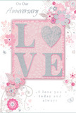The photographed anniversary card carries a sense of treasured intimacy, as if it were meant to be propped beside a freshly arranged vase of roses in a Tooting kitchen on a special evening. At its heart lies the word LOVE, formed in raised, glitter-touched letters that curve softly and invite the fingertips to linger. The glitter is a refined blend of pale silver and pearly white, giving the letters a soft glow that changes gently with the angle of the light, rather than a harsh sparkle. The O is transformed into a shimmering heart, subtly more silver-toned and textured than the surrounding letters, making it the emotional pivot of the piece. Around this central motif, clusters of delicate blossoms unfurl, their petals in shades of blush pink and soft mauve, applied with a light, almost translucent quality that feels like watercolour blooming across the card. Slender vines, curls, and leaves meander around the flowers, echoing the organic lines of stems and foliage a florist might bend and shape when creating an anniversary bouquet for a home near Tooting Bec Common. Tiny flourishes-floating petals, spiral swirls, and discreet butterfly silhouettes-pepper the background, adding a touch of whimsy and movement. The base colour is a muted, gentle pink, offering a warm backdrop for the white, blush, and silver detailing. Phrases such as On Our Anniversary and I love you today and always are written in an elegant, flowing script, the ink hovering gracefully above the floral motifs. Altogether, the card gives the impression of a softly spoken promise: a quiet yet deeply heartfelt way to honour an ongoing journey of love shared in Tooting.